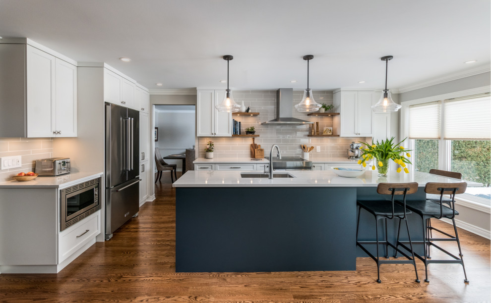 Photo of a transitional kitchen in Ottawa with an undermount sink, shaker cabinets, white cabinets, grey splashback, stainless steel appliances, medium hardwood floors, with island and grey benchtop.