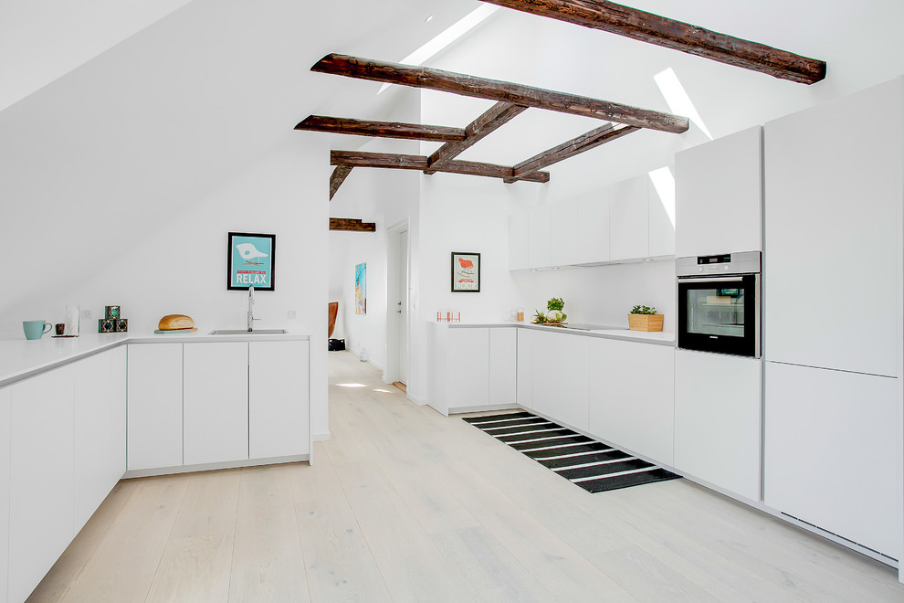 Photo of a scandinavian kitchen in Copenhagen with an undermount sink, flat-panel cabinets, white cabinets, stainless steel appliances and light hardwood floors.