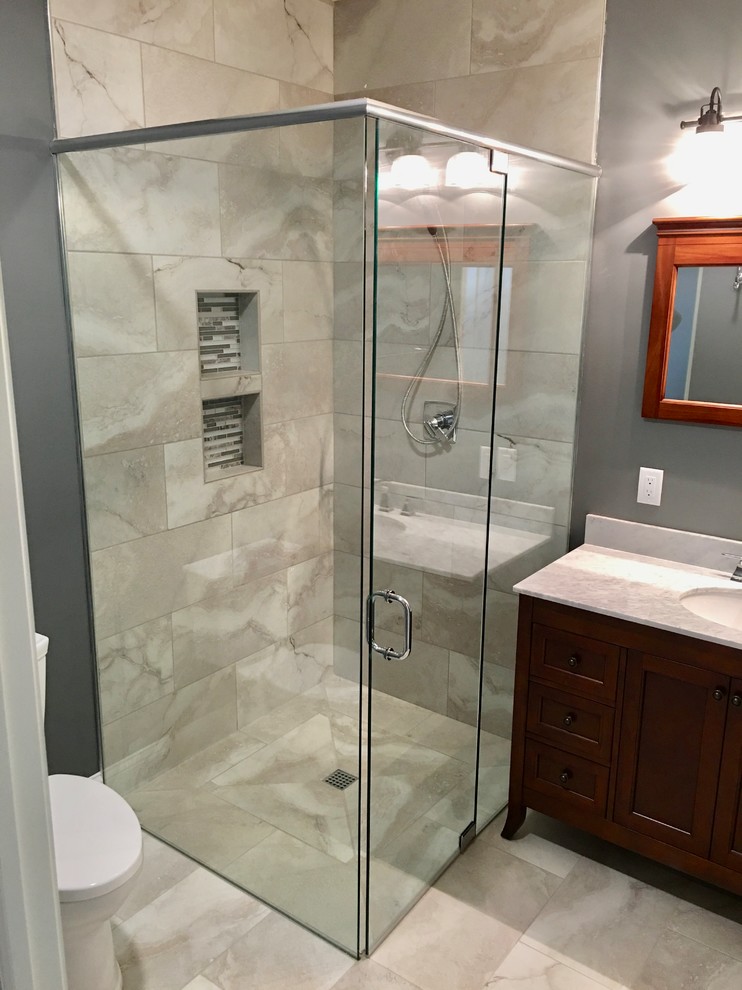 This is an example of a small country master bathroom in Austin with shaker cabinets, dark wood cabinets, a curbless shower, a two-piece toilet, beige tile, porcelain tile, grey walls, porcelain floors, an undermount sink, marble benchtops, beige floor, a hinged shower door and white benchtops.