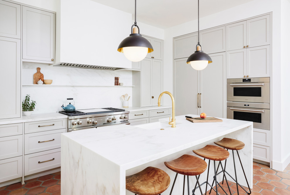 Klassisk inredning av ett avskilt, mellanstort vit vitt l-kök, med en rustik diskho, skåp i shakerstil, grå skåp, marmorbänkskiva, vitt stänkskydd, stänkskydd i marmor, integrerade vitvaror, klinkergolv i terrakotta, en köksö och brunt golv