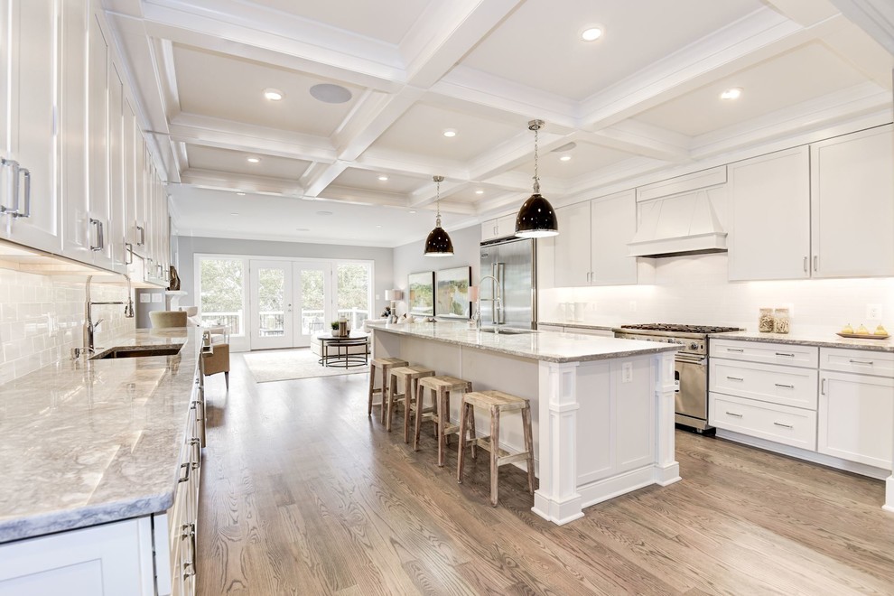 This is an example of a mid-sized transitional galley open plan kitchen in DC Metro with an undermount sink, shaker cabinets, white cabinets, granite benchtops, white splashback, ceramic splashback, stainless steel appliances, medium hardwood floors, with island, brown floor and beige benchtop.