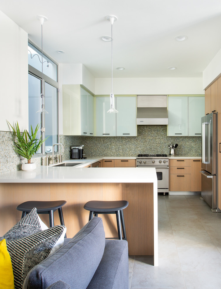 Photo of a contemporary u-shaped open plan kitchen in Los Angeles with an undermount sink, flat-panel cabinets, light wood cabinets, grey splashback, stainless steel appliances, a peninsula, grey floor and white benchtop.