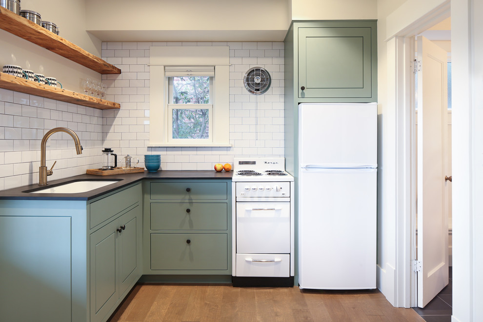 Photo of a small contemporary l-shaped kitchen in Seattle with an undermount sink, flat-panel cabinets, turquoise cabinets, white splashback, subway tile splashback, white appliances, no island, brown floor and black benchtop.