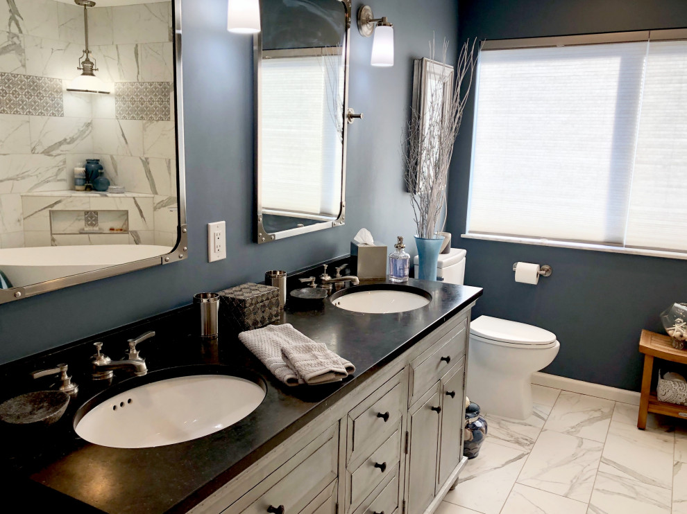 Mid-sized eclectic master bathroom in San Francisco with furniture-like cabinets, grey cabinets, a freestanding tub, a shower/bathtub combo, a one-piece toilet, white tile, porcelain tile, blue walls, porcelain floors, an undermount sink, onyx benchtops, white floor, a hinged shower door and black benchtops.