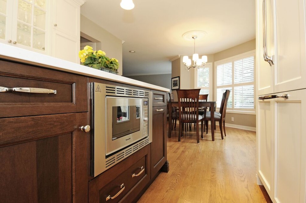 Inspiration for a mid-sized transitional l-shaped medium tone wood floor kitchen remodel in Ottawa with a double-bowl sink, recessed-panel cabinets, white cabinets, quartz countertops, gray backsplash, stone tile backsplash, stainless steel appliances and an island