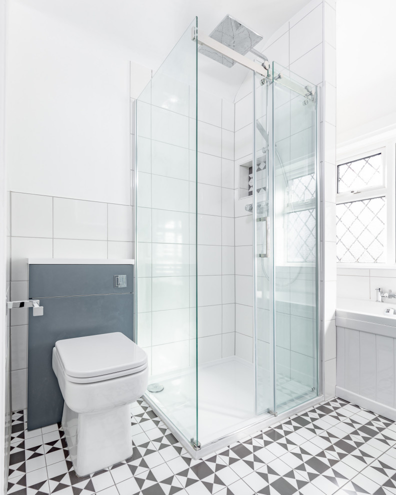 Mid-sized traditional kids bathroom in London with blue cabinets, a drop-in tub, an open shower, a two-piece toilet, white tile, white walls, ceramic floors, multi-coloured floor, a sliding shower screen, a niche, a single vanity and a freestanding vanity.