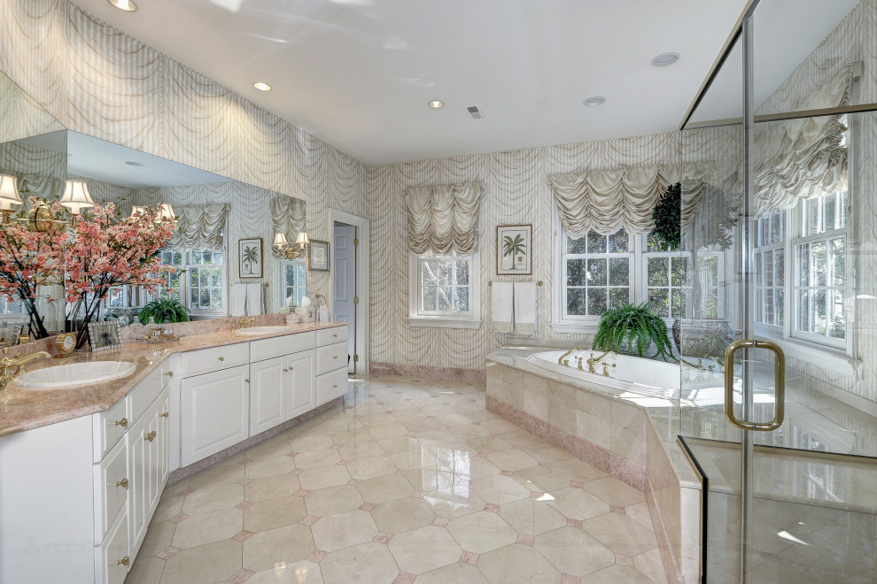 Expansive traditional master bathroom in DC Metro with raised-panel cabinets, white cabinets, a corner tub, a corner shower, beige walls, marble floors, a drop-in sink, marble benchtops, beige floor, a hinged shower door, pink benchtops, a shower seat, a double vanity and a built-in vanity.