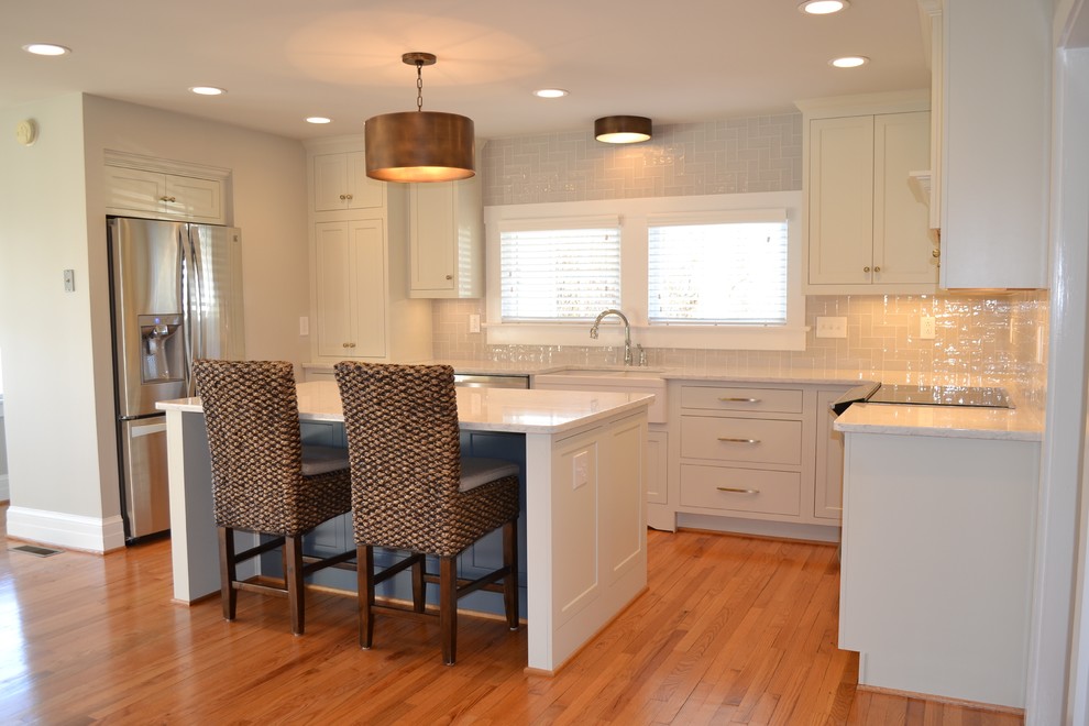 Inspiration for a mid-sized transitional u-shaped light wood floor open concept kitchen remodel with a farmhouse sink, recessed-panel cabinets, white cabinets, quartz countertops, beige backsplash, ceramic backsplash, stainless steel appliances and an island