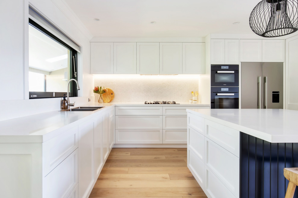 Design ideas for a large beach style l-shaped kitchen pantry in Sydney with a double-bowl sink, shaker cabinets, blue cabinets, quartz benchtops, white splashback, mosaic tile splashback, stainless steel appliances, light hardwood floors, with island, multi-coloured floor, white benchtop and recessed.