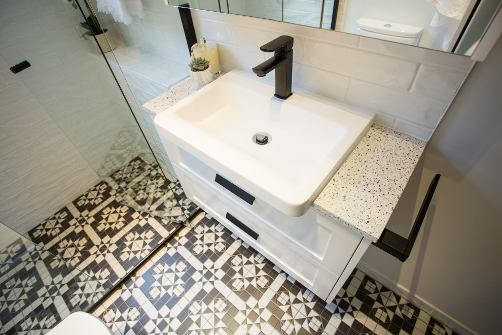 This is an example of a mid-sized contemporary master bathroom in Brisbane with white cabinets, an open shower, a one-piece toilet, white tile, ceramic tile, white walls, a drop-in sink, engineered quartz benchtops, a hinged shower door, white benchtops, shaker cabinets, cement tiles, black floor, a laundry, a single vanity and a built-in vanity.