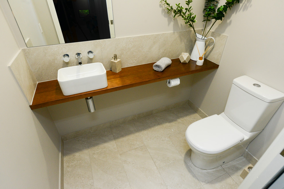 Photo of a small contemporary powder room in Other with open cabinets, beige tile, ceramic tile, beige walls, ceramic floors, a vessel sink, wood benchtops and beige floor.