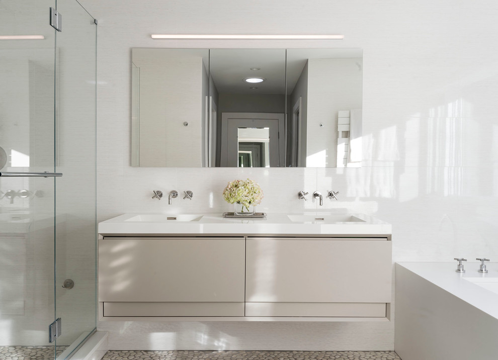 Inspiration for a mid-sized contemporary master bathroom in New York with flat-panel cabinets, beige cabinets, an undermount tub, beige tile, white walls, pebble tile floors, an integrated sink, porcelain tile, solid surface benchtops and a hinged shower door.