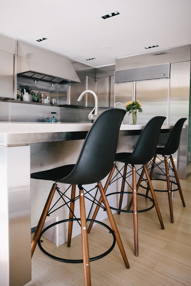 Example of a mid-sized trendy l-shaped light wood floor and beige floor open concept kitchen design with a double-bowl sink, flat-panel cabinets, stainless steel cabinets, stainless steel countertops, metallic backsplash, stainless steel appliances and an island