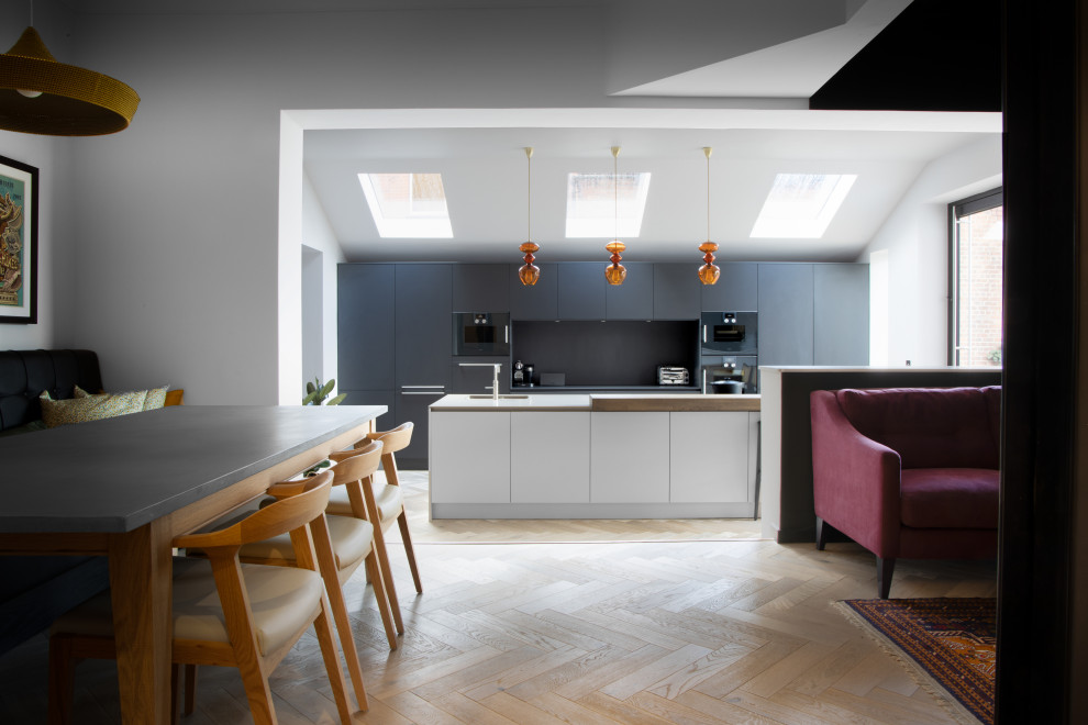 This is an example of a large scandinavian galley open plan kitchen in Cheshire with an integrated sink, flat-panel cabinets, black cabinets, quartzite benchtops, black splashback, black appliances, light hardwood floors, with island and white benchtop.