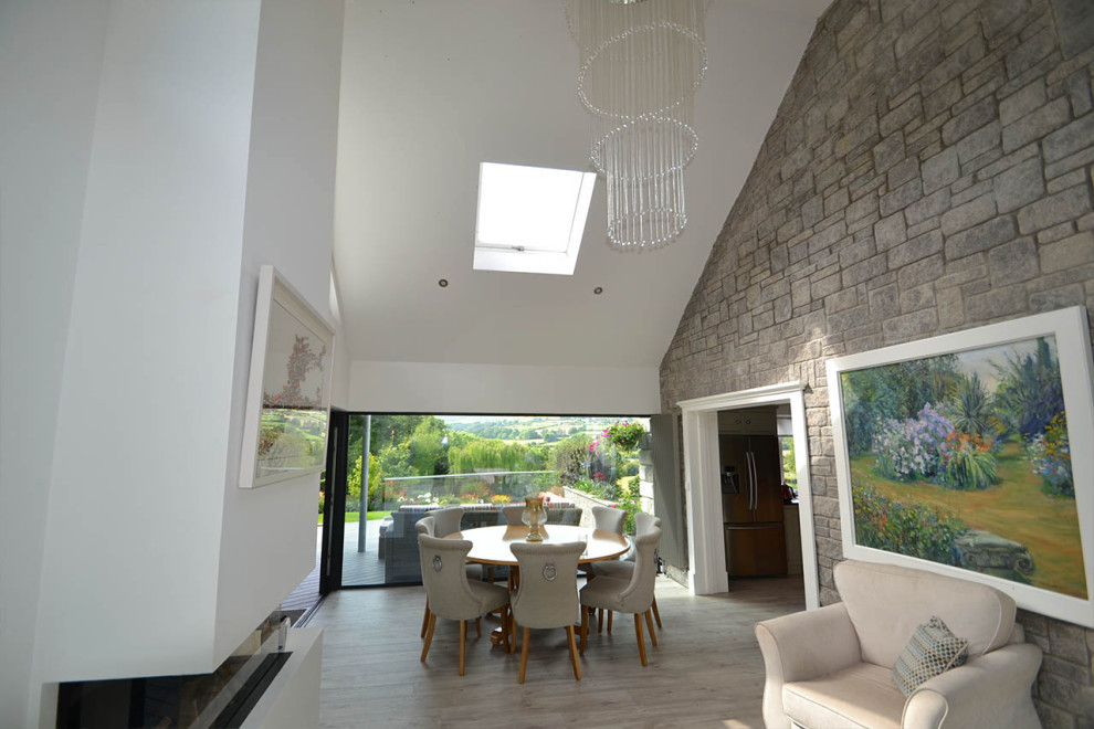 This is an example of a mid-sized contemporary open plan dining in Other with white walls, light hardwood floors, a standard fireplace, a plaster fireplace surround, grey floor, vaulted and brick walls.