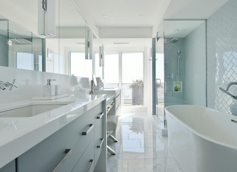 This is an example of a beach style master bathroom in Ottawa with flat-panel cabinets, blue cabinets, a freestanding tub, a corner shower, blue tile, subway tile, white walls, marble floors, an undermount sink, white floor, a hinged shower door and white benchtops.