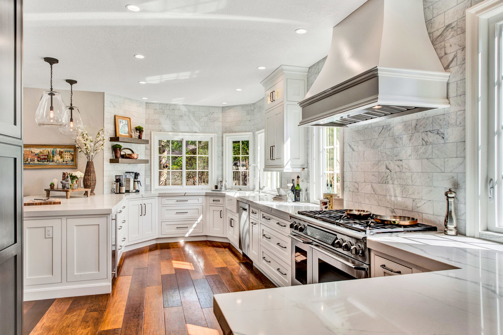 Design ideas for a transitional u-shaped kitchen in Orange County with a farmhouse sink, beaded inset cabinets, white cabinets, white splashback, stainless steel appliances, dark hardwood floors, a peninsula, brown floor and white benchtop.