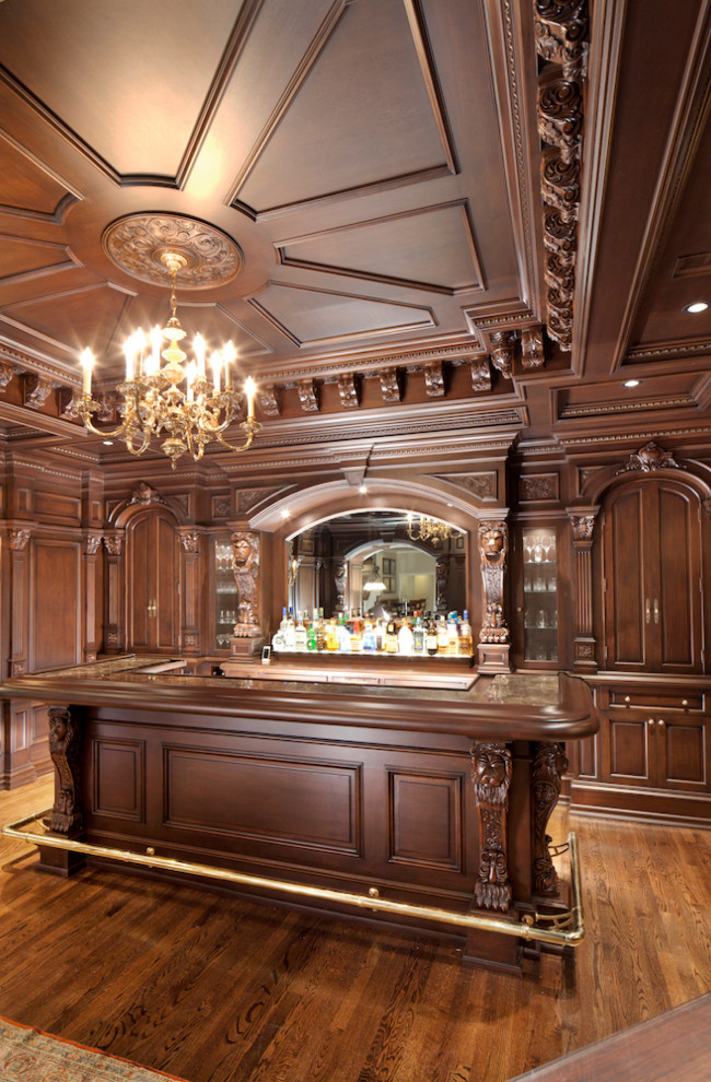 This is an example of a large traditional u-shaped seated home bar in New York with a drop-in sink, shaker cabinets, brown cabinets, quartz benchtops, brown splashback, engineered quartz splashback, medium hardwood floors, brown floor and brown benchtop.