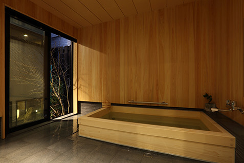 This is an example of a small asian master bathroom in Kyoto with beaded inset cabinets, light wood cabinets, a hot tub, an open shower, a one-piece toilet, gray tile, stone tile, grey walls, porcelain floors, an undermount sink, solid surface benchtops, grey floor, an open shower and white benchtops.