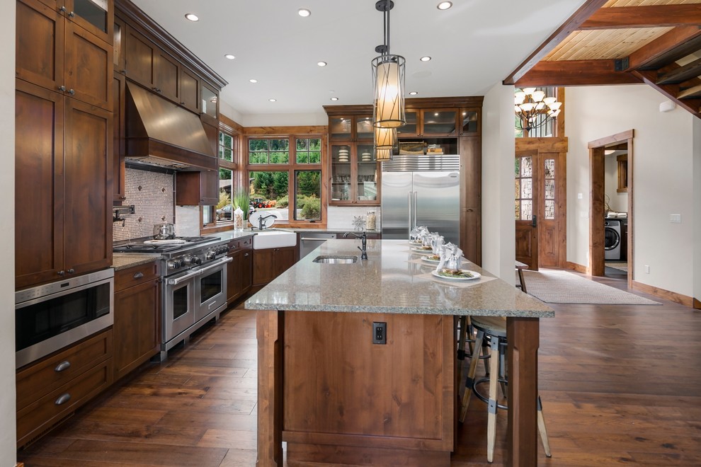 Design ideas for a country l-shaped open plan kitchen in Seattle with recessed-panel cabinets, dark wood cabinets, white splashback, stainless steel appliances, dark hardwood floors, with island and brown floor.