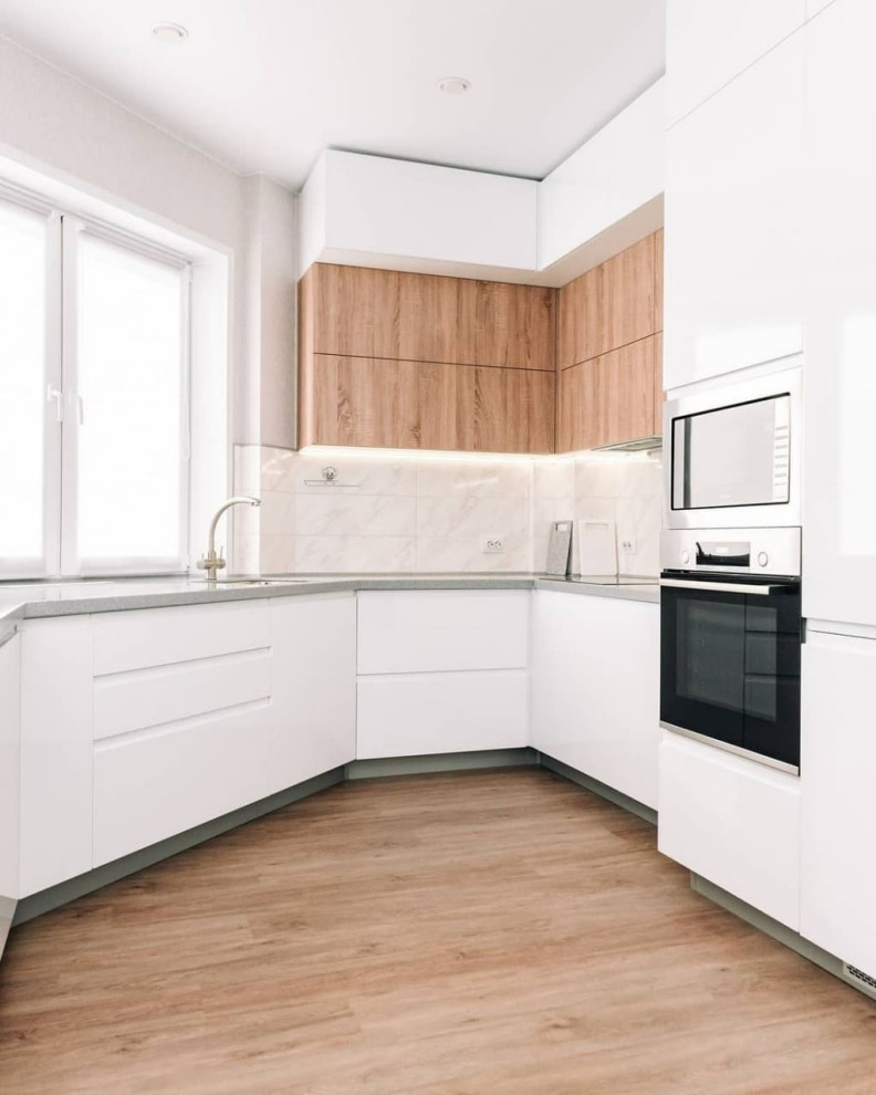 Inspiration for a large contemporary u-shaped eat-in kitchen in Novosibirsk with an undermount sink, flat-panel cabinets, white cabinets, solid surface benchtops, white splashback, glass sheet splashback, stainless steel appliances, medium hardwood floors, a peninsula, brown floor and grey benchtop.