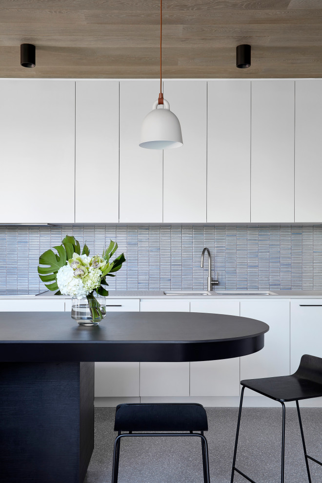 Design ideas for a mid-sized contemporary galley eat-in kitchen in Melbourne with a drop-in sink, flat-panel cabinets, white cabinets, solid surface benchtops, blue splashback, ceramic splashback, black appliances, concrete floors, with island, grey floor and black benchtop.