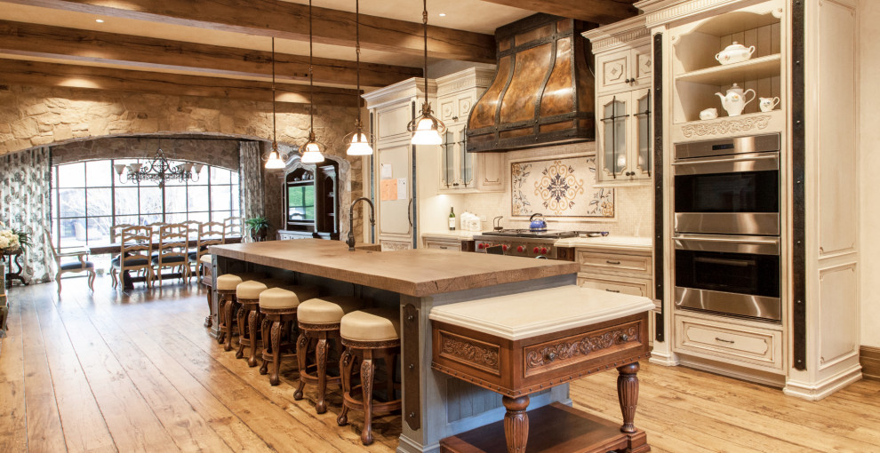 Eat-in kitchen - large french country u-shaped medium tone wood floor, brown floor and exposed beam eat-in kitchen idea in New York with a farmhouse sink, shaker cabinets, beige cabinets, quartz countertops, beige backsplash, quartz backsplash, stainless steel appliances, an island and beige countertops