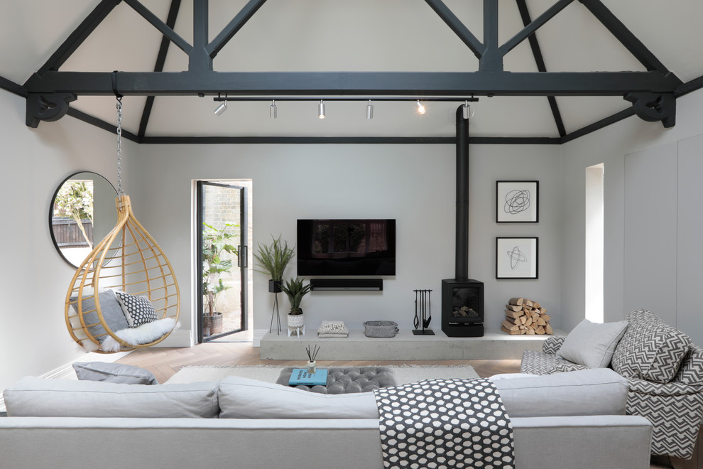 Inspiration for a transitional living room in Hertfordshire with grey walls, light hardwood floors, a wood stove, a metal fireplace surround, a wall-mounted tv and beige floor.
