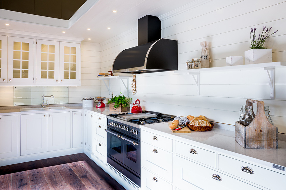 Photo of a mid-sized country l-shaped kitchen in Gothenburg with open cabinets, white cabinets, white splashback, black appliances, medium hardwood floors, a double-bowl sink, granite benchtops and no island.