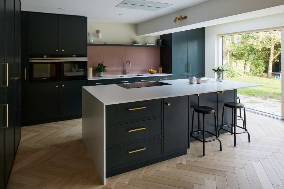 Photo of a large contemporary l-shaped eat-in kitchen in Kent with recessed-panel cabinets, green cabinets, quartz benchtops, pink splashback, glass sheet splashback, stainless steel appliances, with island and white benchtop.