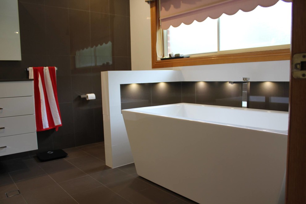 Contemporary bathroom in Sydney with flat-panel cabinets, white cabinets, a freestanding tub and black tile.