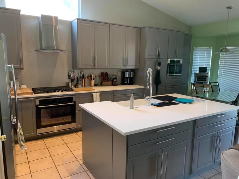 Transitional l-shaped porcelain tile and beige floor open concept kitchen photo in Phoenix with a farmhouse sink, raised-panel cabinets, gray cabinets, solid surface countertops, stainless steel appliances, an island and white countertops