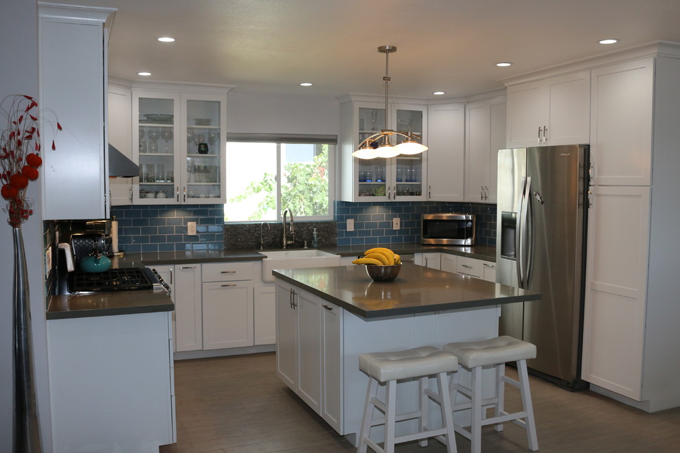 Inspiration for a mid-sized contemporary u-shaped eat-in kitchen in San Diego with a farmhouse sink, shaker cabinets, white cabinets, solid surface benchtops, blue splashback, glass tile splashback, stainless steel appliances, ceramic floors and with island.