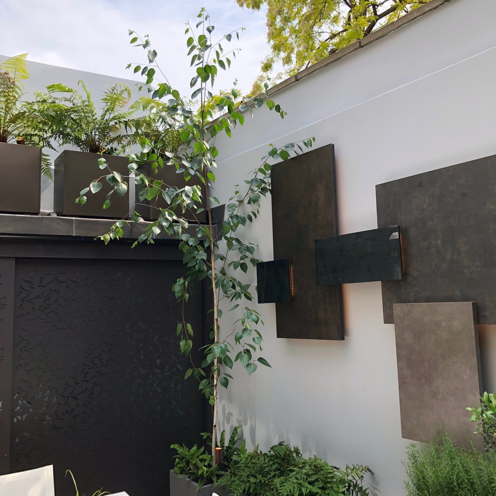 This is an example of a small contemporary backyard partial sun garden in London with natural stone pavers.