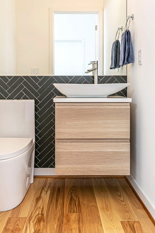 Réalisation d'un petit WC et toilettes design en bois clair avec un placard à porte plane, un carrelage noir, un plan de toilette en marbre et meuble-lavabo suspendu.