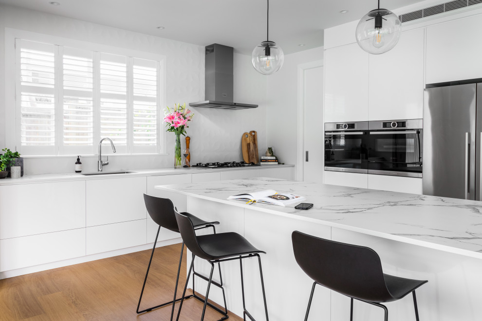Large contemporary l-shaped kitchen/diner in Auckland with a submerged sink, recessed-panel cabinets, white cabinets, engineered stone countertops, white splashback, porcelain splashback, stainless steel appliances, light hardwood flooring, an island and yellow worktops.