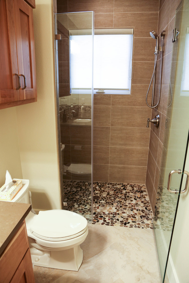 Inspiration for a mid-sized 3/4 bathroom in Austin with shaker cabinets, light wood cabinets, an alcove shower, a one-piece toilet, multi-coloured tile, pebble tile, beige walls, travertine floors and solid surface benchtops.