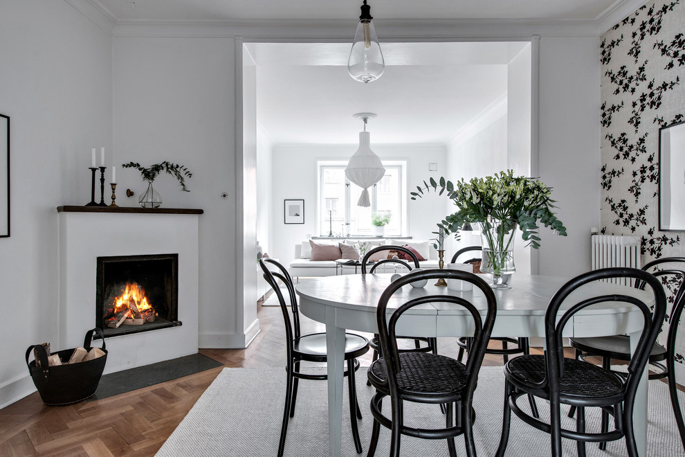 Photo of a scandinavian open plan dining in Gothenburg with white walls, medium hardwood floors, a standard fireplace and brown floor.