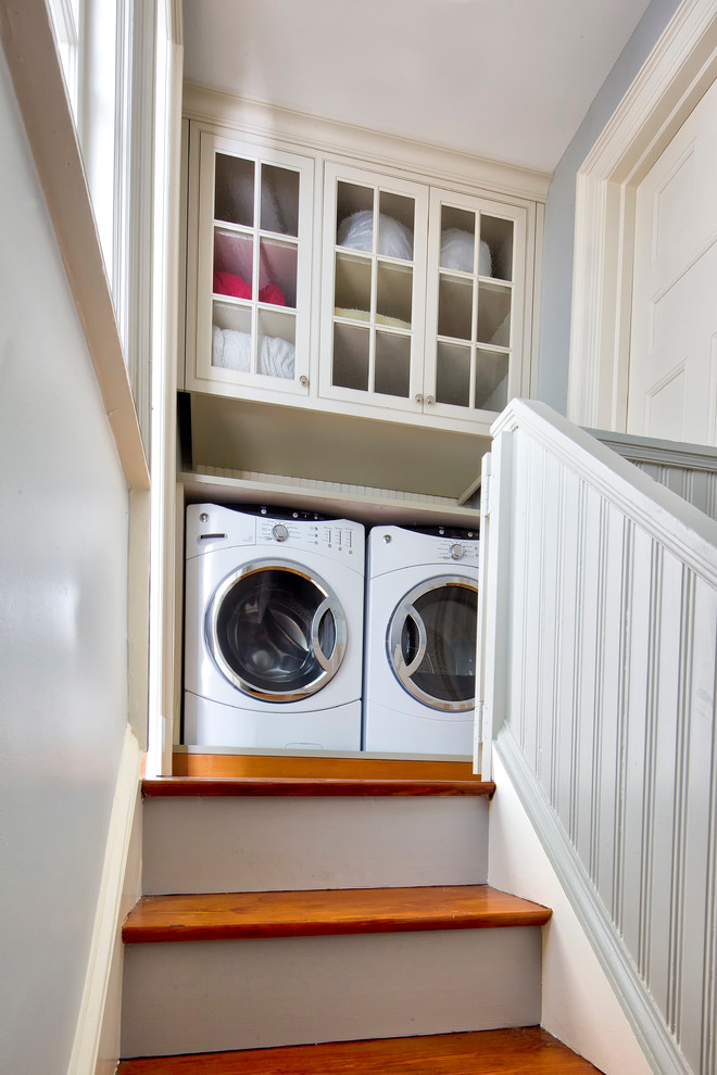 Photo of a traditional laundry cupboard in New York with glass-front cabinets, beige cabinets and a side-by-side washer and dryer.