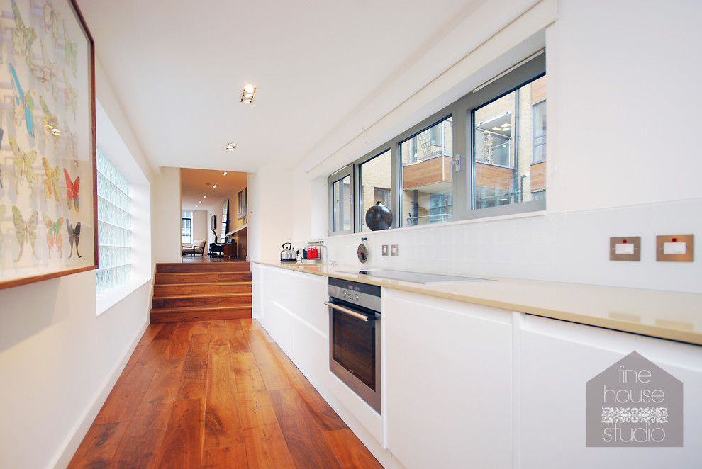 Photo of an expansive contemporary single-wall open plan kitchen in Gloucestershire with a single-bowl sink, shaker cabinets, white cabinets, limestone worktops, white splashback, glass sheet splashback, stainless steel appliances, dark hardwood flooring and no island.