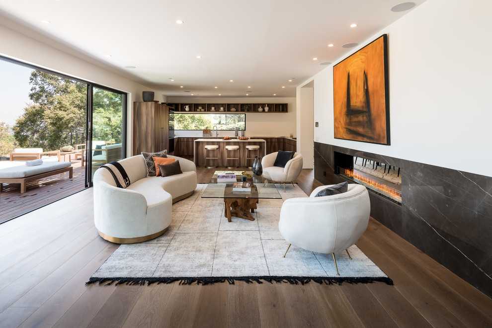 Design ideas for an expansive contemporary open concept living room in Los Angeles with white walls, medium hardwood floors, a two-sided fireplace, a stone fireplace surround, a concealed tv and brown floor.