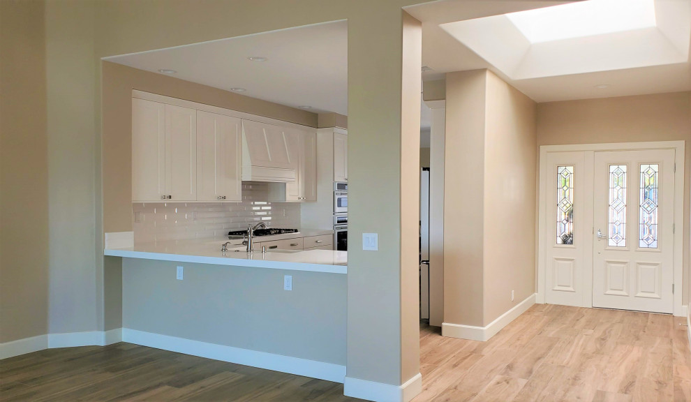 Eat-in kitchen - small transitional u-shaped porcelain tile eat-in kitchen idea in Orange County with a farmhouse sink, shaker cabinets, white cabinets, quartzite countertops, white backsplash, subway tile backsplash, white appliances and white countertops
