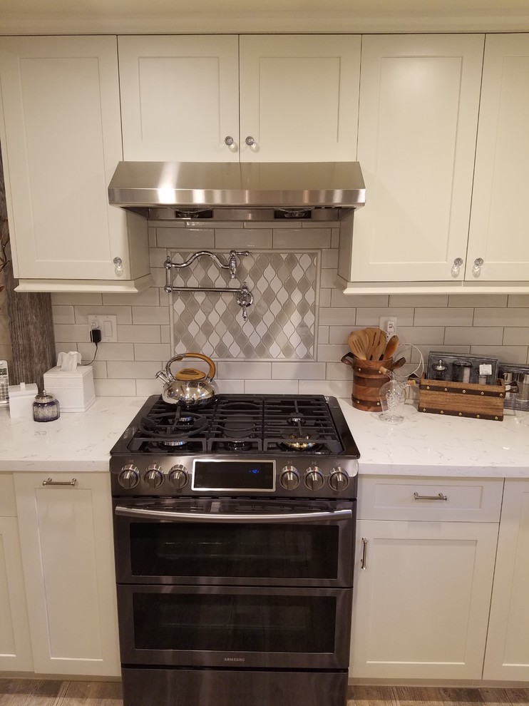 Mid-sized country l-shaped separate kitchen in Los Angeles with a farmhouse sink, shaker cabinets, white cabinets, quartz benchtops, white splashback, subway tile splashback, stainless steel appliances, light hardwood floors, with island and brown floor.