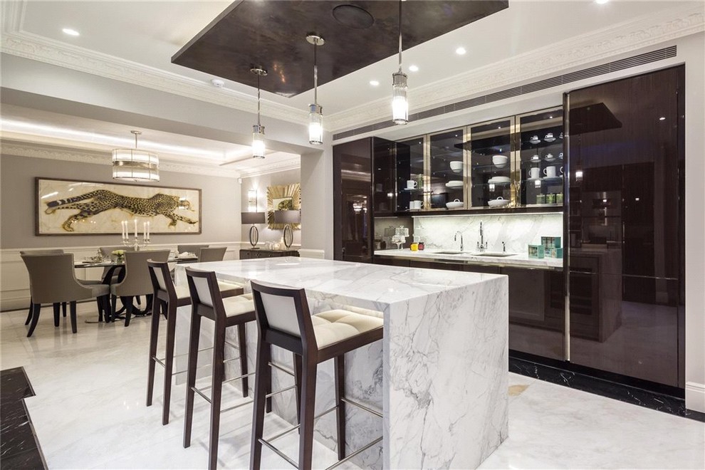 Contemporary galley open plan kitchen in London with an undermount sink, glass-front cabinets, brown cabinets, marble benchtops, white splashback, marble splashback, marble floors and with island.