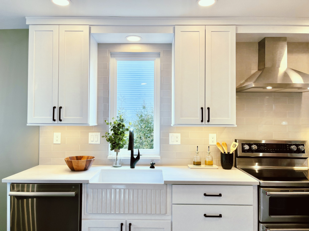 Mid-sized transitional l-shaped vinyl floor and black floor eat-in kitchen photo with a farmhouse sink, shaker cabinets, white cabinets, quartz countertops, gray backsplash, ceramic backsplash, stainless steel appliances, a peninsula and gray countertops