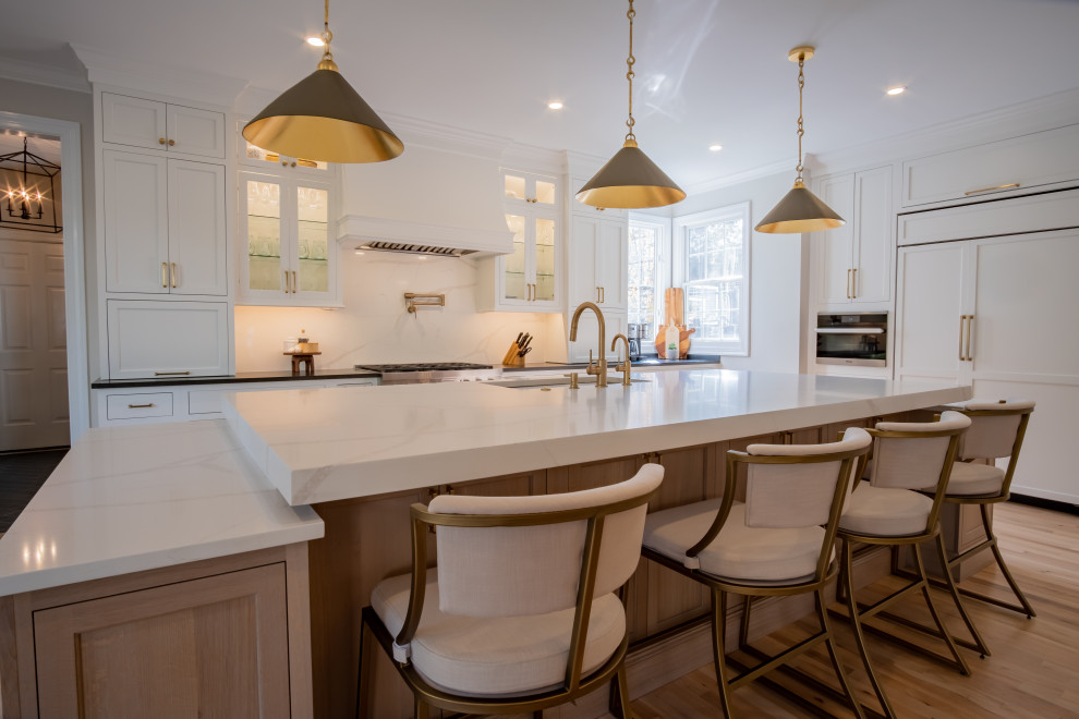 Large traditional l-shaped eat-in kitchen in DC Metro with an undermount sink, beaded inset cabinets, white cabinets, quartz benchtops, white splashback, engineered quartz splashback, stainless steel appliances, light hardwood floors, with island, brown floor, white benchtop and wallpaper.