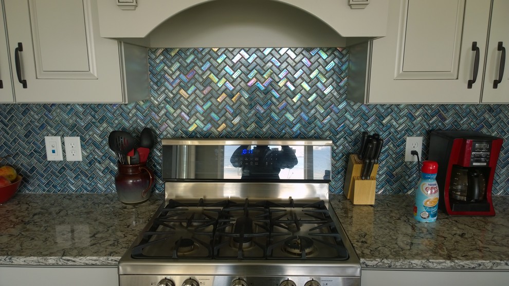 Example of a large minimalist eat-in kitchen design with white cabinets, blue backsplash, glass tile backsplash, stainless steel appliances and an island
