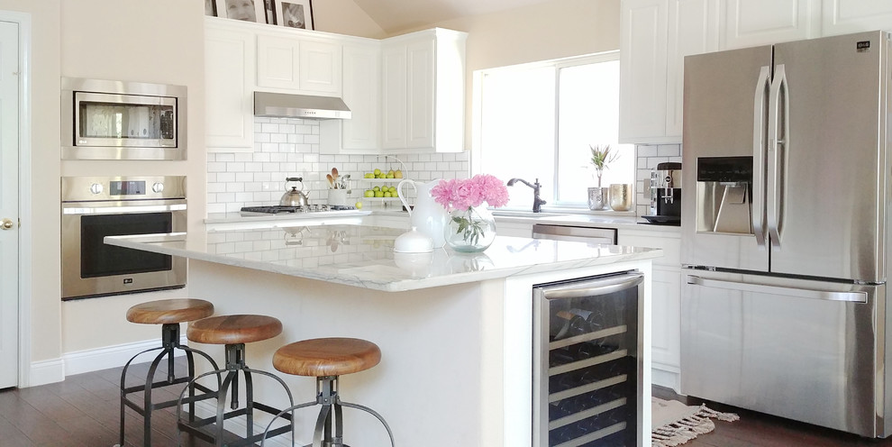 This is an example of a mid-sized scandinavian l-shaped kitchen in Austin with an undermount sink, raised-panel cabinets, white cabinets, marble benchtops, white splashback, subway tile splashback, stainless steel appliances, dark hardwood floors, with island, brown floor and white benchtop.