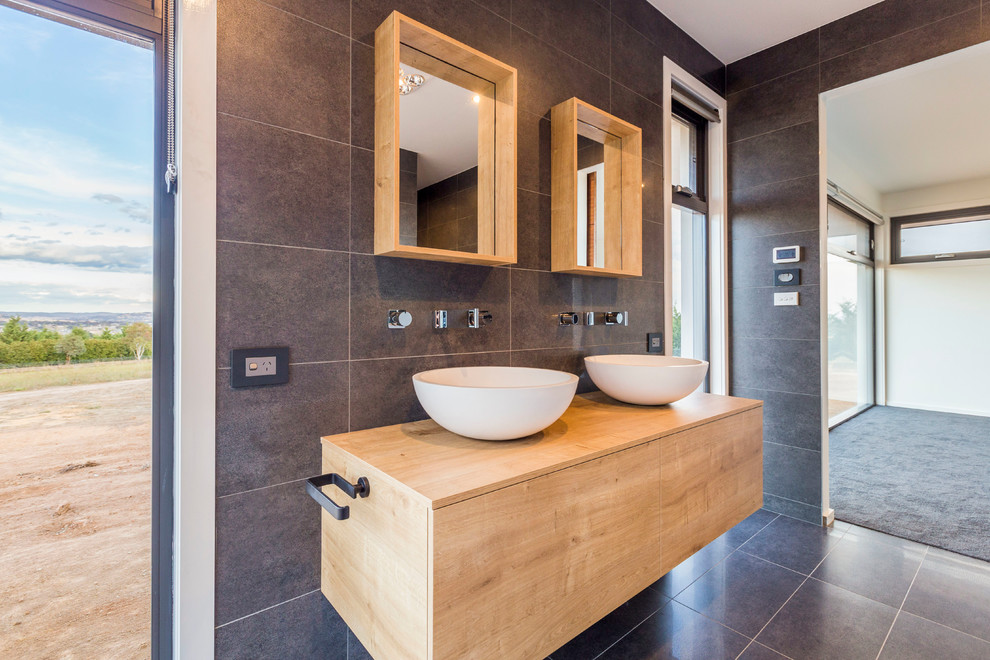 Photo of a large contemporary master bathroom in Canberra - Queanbeyan with a trough sink, open cabinets, light wood cabinets, wood benchtops, a freestanding tub, gray tile, ceramic tile, grey walls and ceramic floors.