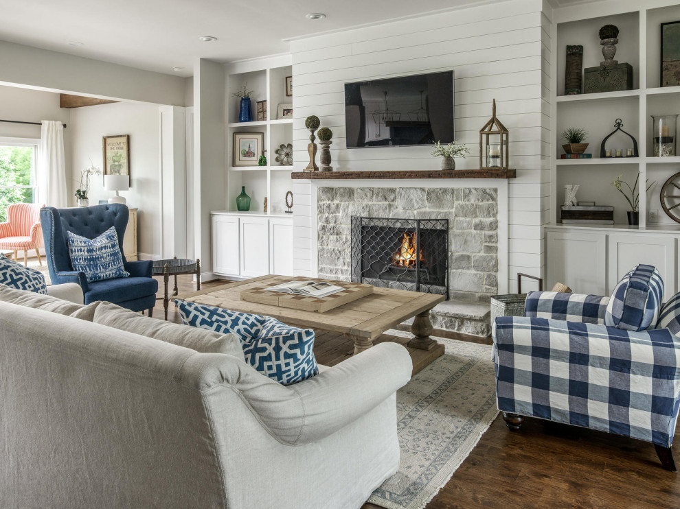 Inspiration for a large country open concept living room in Nashville with white walls, medium hardwood floors, a standard fireplace, a stone fireplace surround, a wall-mounted tv and brown floor.